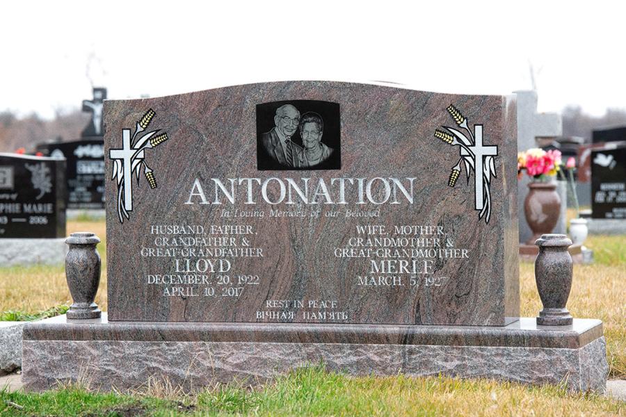Antonation, a traditional style double memorial in Paradiso granite.  Customizations to this traditional memorial is all sides polished, a matching polish top 2" margin Paradiso base, one impact etched portrait on a Midnight Black granite insert, two matching granite vases and gold paint embellishments.  