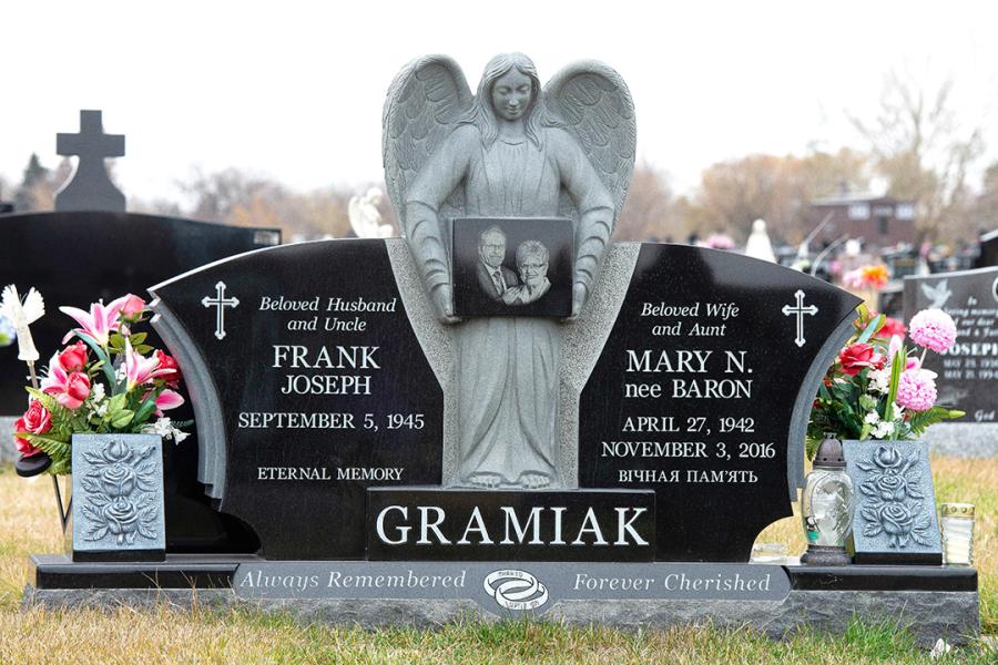 Gramiak, Midnight Black custom design sculptured Angel Memorial installed in Holy Family cemetery. Featured add-ons, Flowerless vases, gold paint detailing, and a Diamond Impact Etched portrait all on a Matching custom design 2" margin polish top base with panel. Located in Holy Family Cemetery.  